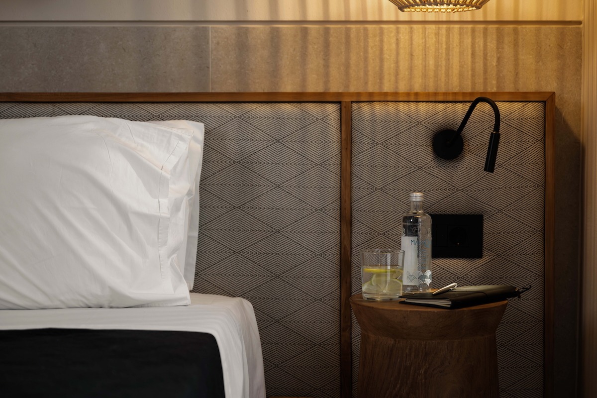 Luxury villa bedroom detail showing bedside table, reading lamp, water bottle, and textured headboard in Rhodes