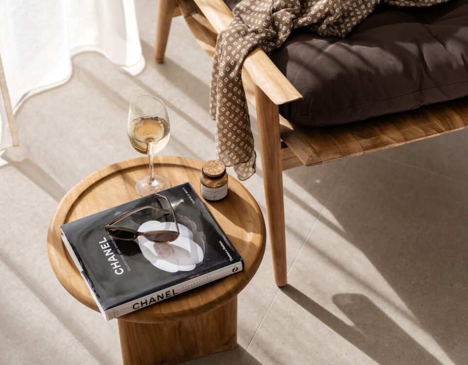 Luxury villa interior detail with wooden lounge chair, side table, book, and glass of wine in Rhodes